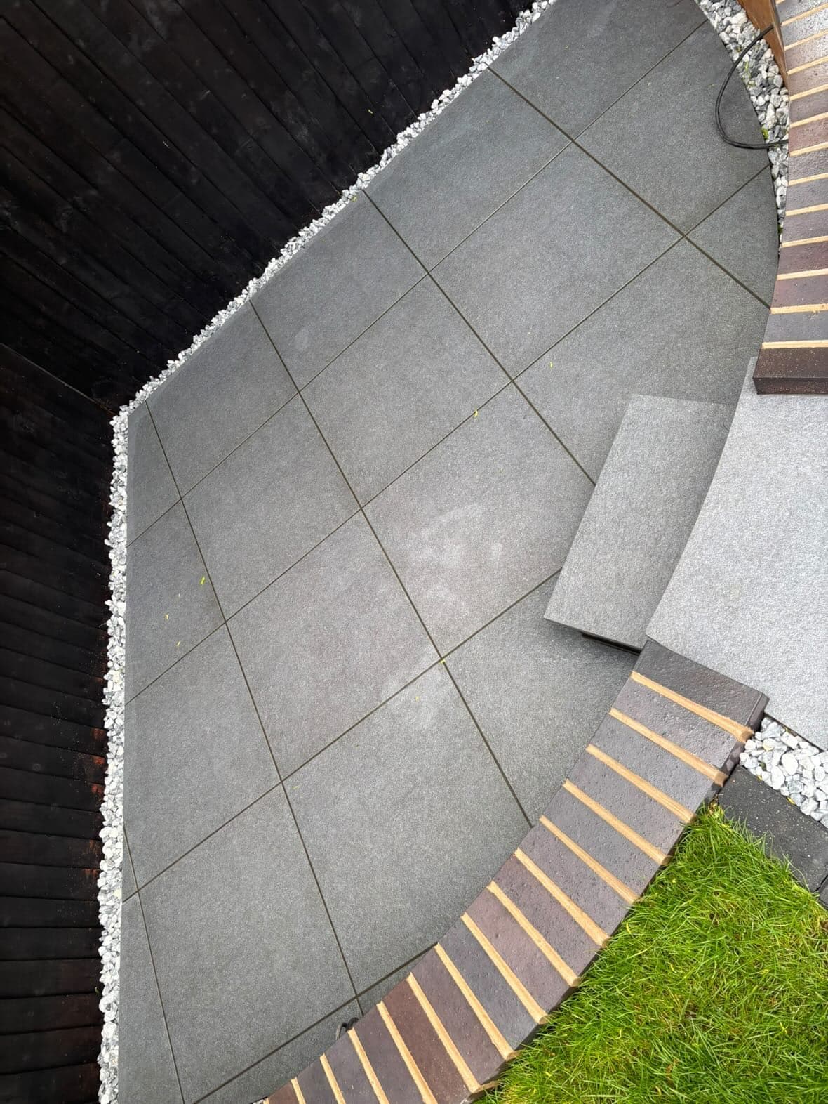 Finished curved porcelain patio with brick edging viewed from above